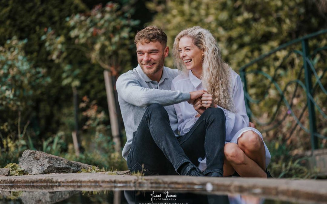 A happy couple being photographed sitting by a pond at Braintree and Bocking Public Gardens