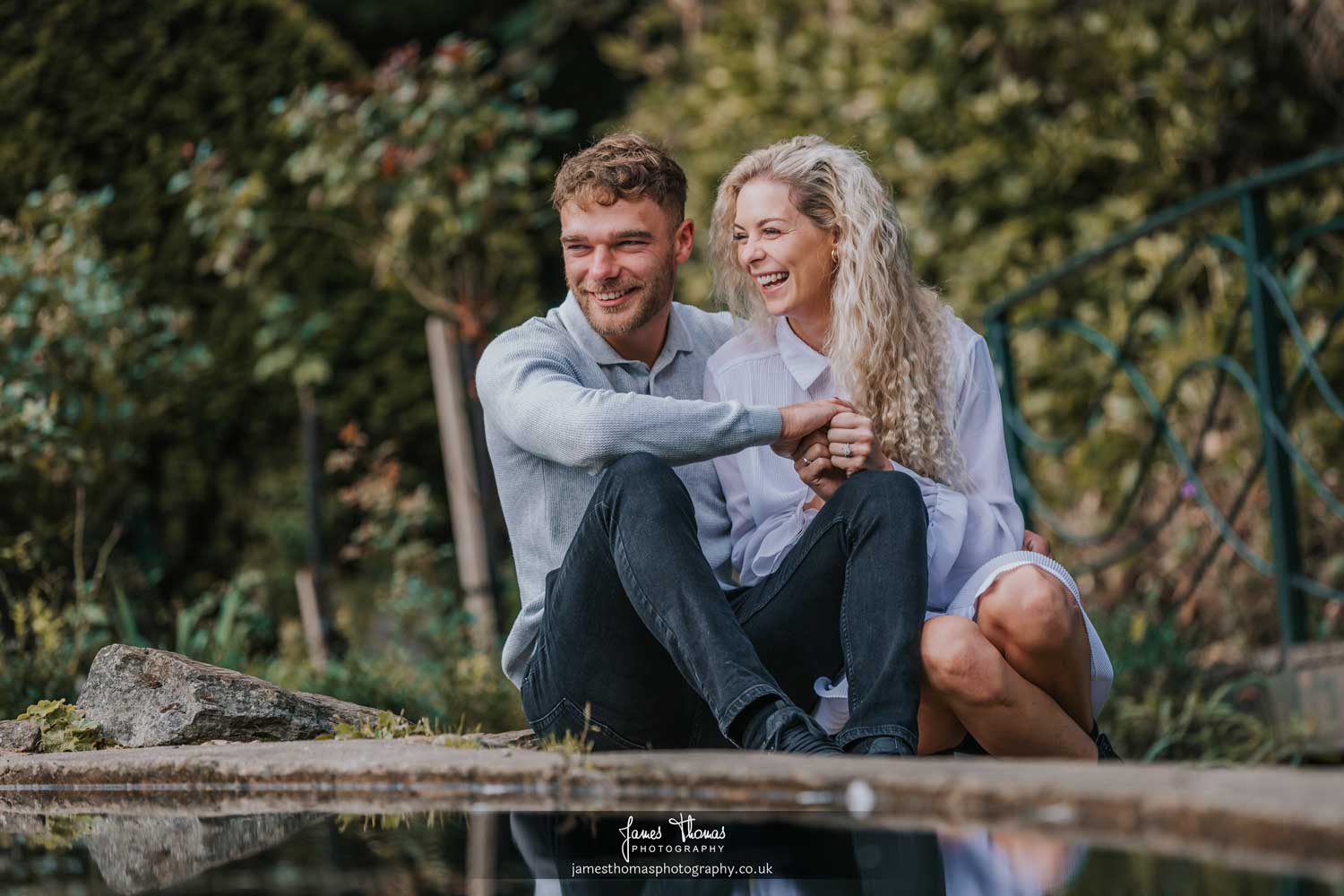 A happy couple being photographed sitting by a pond at Braintree and Bocking Public Gardens