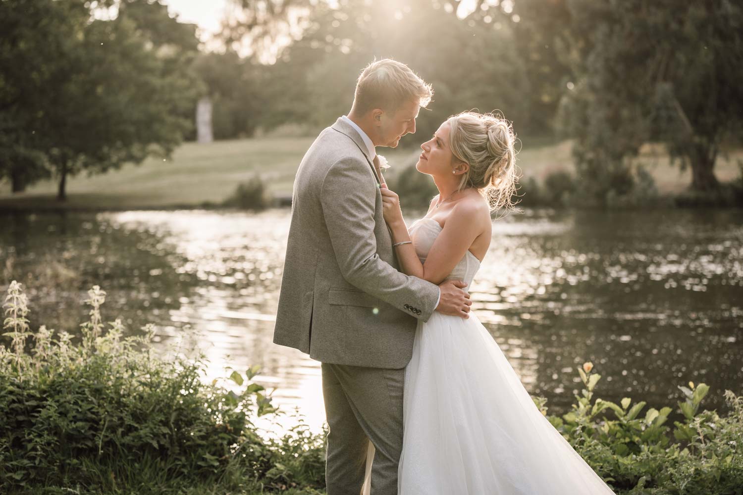 Bride and groom by the lake at Wivenhoe House during golden hour.